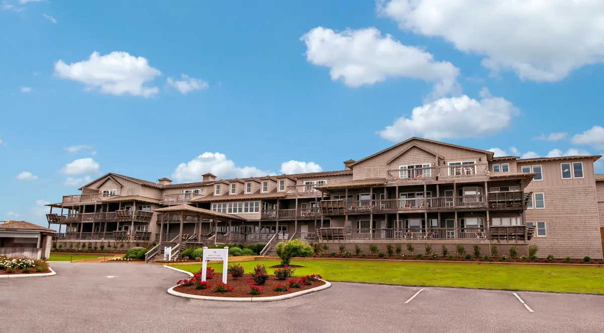 This image captures a modern building facade with several private balconies overlooking beautifully landscaped gardens. The balconies, some furnished with chairs, hint at private, tranquil spaces ideal for relaxation and enjoying the view. The soft light suggests either early morning or late afternoon, evoking times ideal for coffee at sunrise or sunset cocktails.