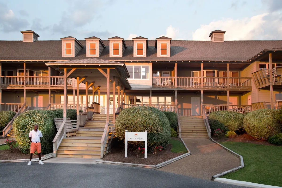 This image shows the inviting front entrance of the property, featuring a staircase bordered by manicured bushes and a prominent sign reading 'A Beach House'. The porch area looks tranquil and offers views of the surrounding landscape, suggesting a relaxing spot to enjoy the outdoors.